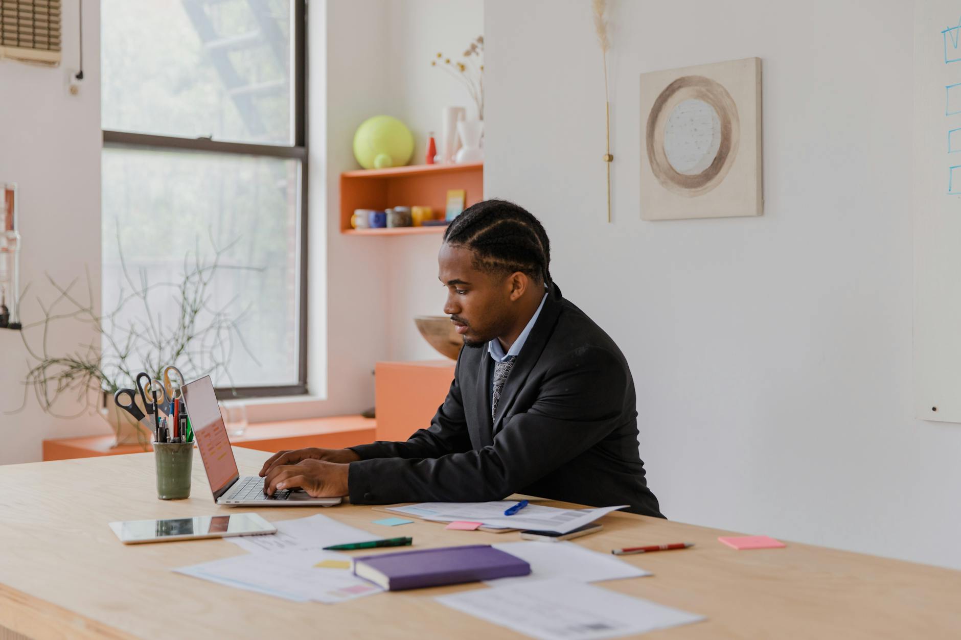 Professional businessman with braided hair working on a laptop at an office desk. - Mattress Miracle Brantford